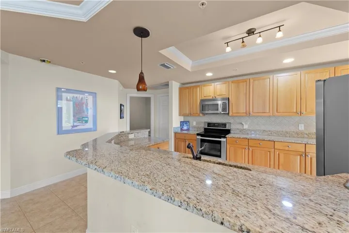 Kitchen with a raised ceiling, stainless steel appliances, decorative light fixtures, and ornamental molding