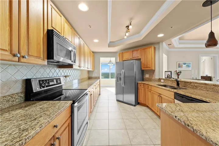 Kitchen featuring crown molding, light stone countertops, appliances with stainless steel finishes, a tray ceiling, and decorative light fixtures