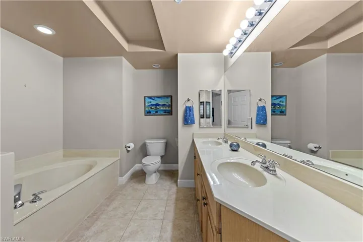 Bathroom featuring a tub, dual vanity, toilet, and tile floors
