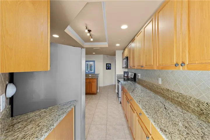 Kitchen with stainless steel appliances, a tray ceiling, light stone counters, backsplash, and light tile floors
