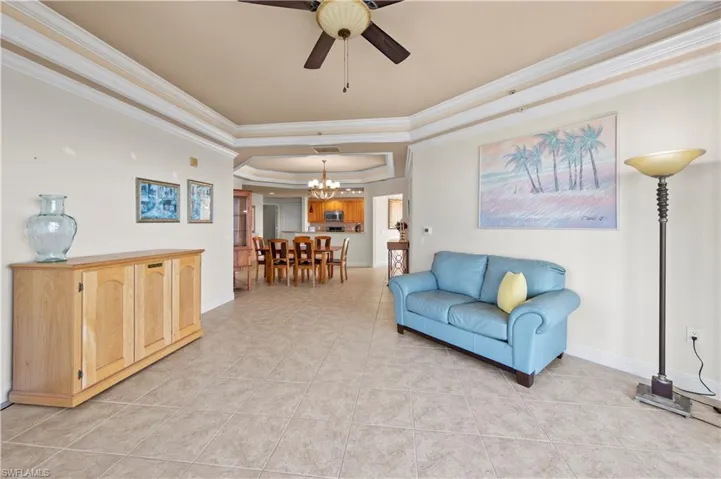 Tiled living room with a raised ceiling, ceiling fan with notable chandelier, and crown molding