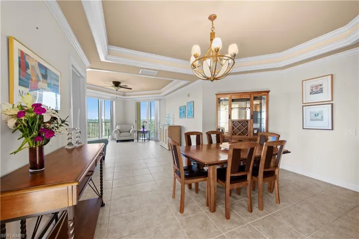 Tiled dining space with crown molding, a raised ceiling, and ceiling fan with notable chandelier