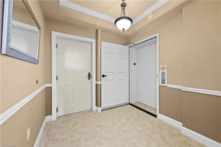 Tiled foyer entrance with crown molding, elevator, and a raised ceiling