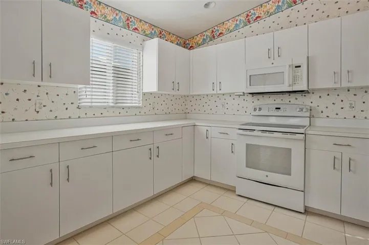 Kitchen with white appliances, light tile patterned flooring, light countertops, and white cabinets