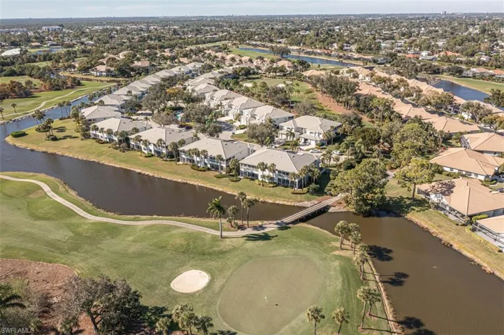 Aerial view of property and surrounding area featuring a golf club, a large body of water, and nearby suburban area