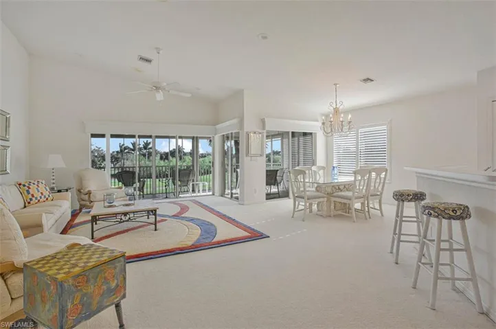 Living room featuring plenty of natural light, light colored carpet, lofted ceiling, a ceiling fan, and a chandelier