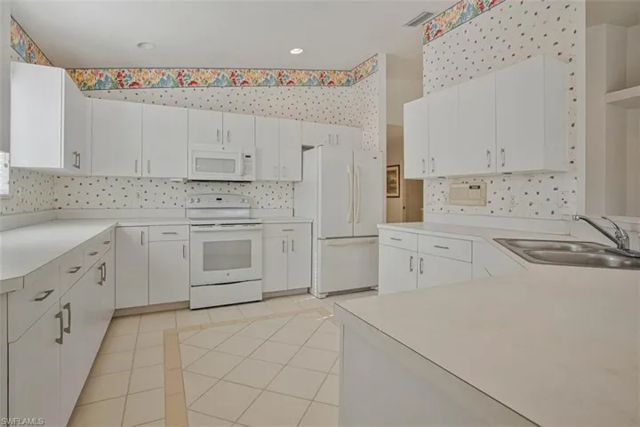 Kitchen with white appliances, white cabinetry, light countertops, wallpapered walls, and recessed lighting