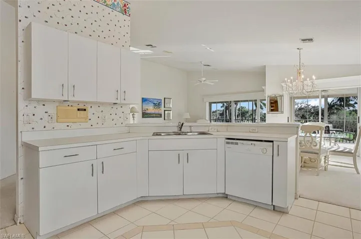 Kitchen featuring light countertops, white cabinets, white dishwasher, a chandelier, and lofted ceiling