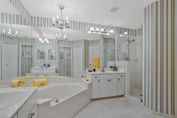 Bathroom featuring wallpapered walls, a stall shower, a garden tub, and two vanities