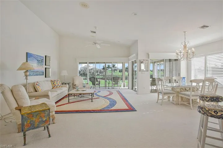 Carpeted living room featuring a chandelier, a ceiling fan, and high vaulted ceiling