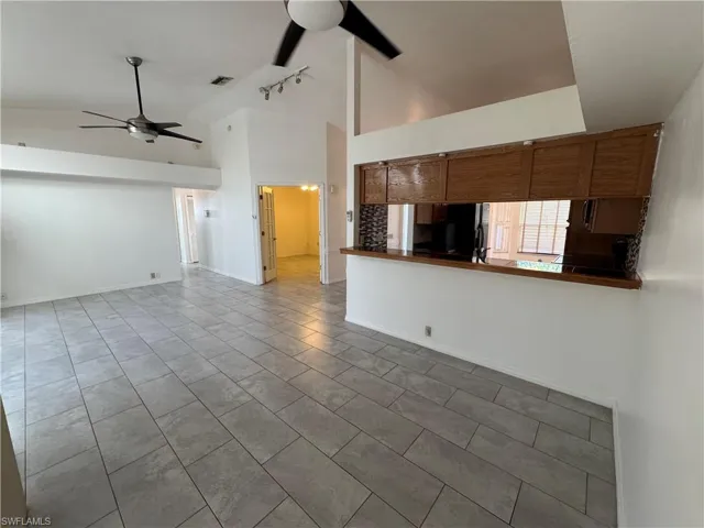 Unfurnished living room with a ceiling fan, high vaulted ceiling, rail lighting, and tile patterned flooring