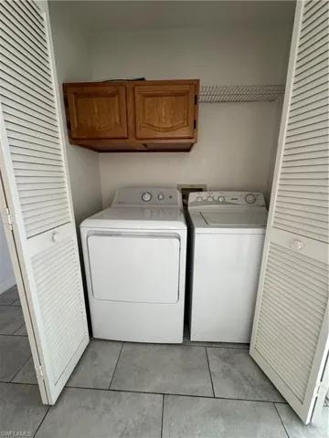 Laundry area featuring cabinet space, light tile patterned floors, and washing machine and clothes dryer