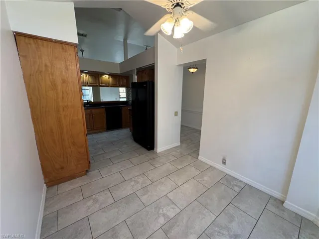 Kitchen with black appliances, dark countertops, ceiling fan, light tile patterned floors, and brown cabinetry