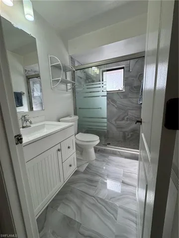 Full bathroom featuring vanity, a marble finish shower, and light marble finish floors