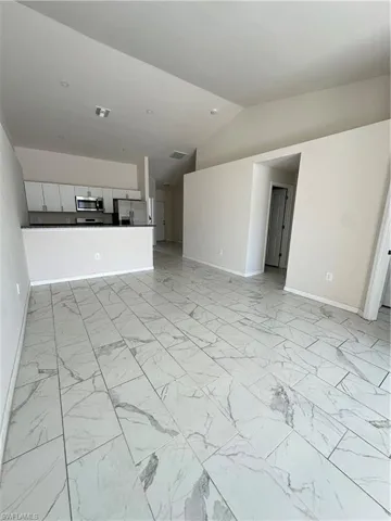 Unfurnished living room featuring lofted ceiling and light marble finish flooring