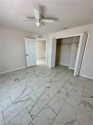 Unfurnished bedroom with a ceiling fan, a closet, and light marble finish floors