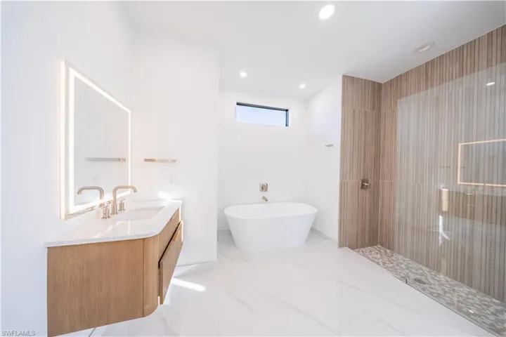 Bathroom featuring vanity, a walk in shower, a freestanding bath, and recessed lighting