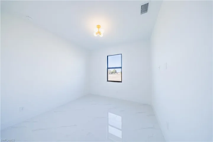 Empty room featuring light marble finish flooring and a chandelier