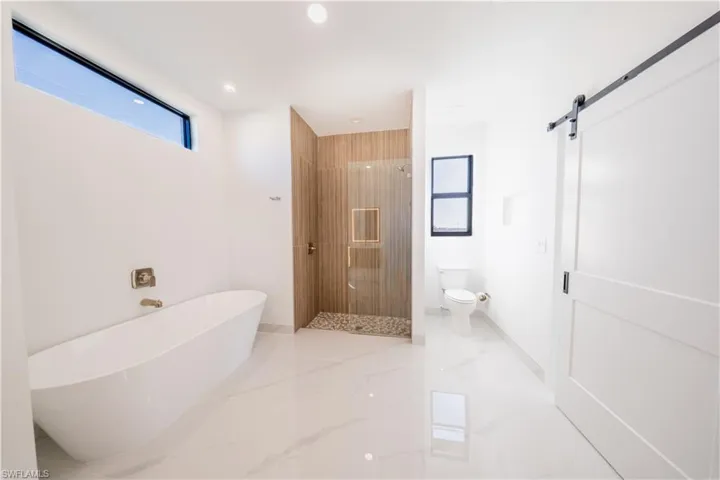 Full bathroom featuring a stall shower, a freestanding tub, light marble finish flooring, and recessed lighting