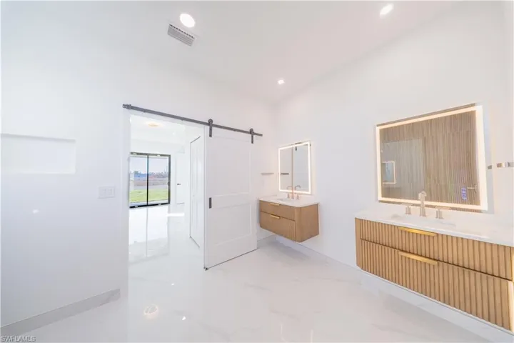 Full bath featuring two vanities, light marble finish floors, and recessed lighting