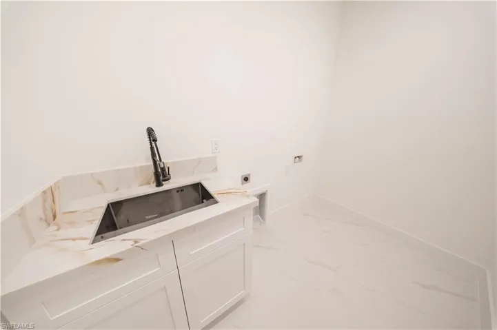 Laundry area featuring electric dryer hookup, cabinet space, light marble finish floors, and hookup for a washing machine
