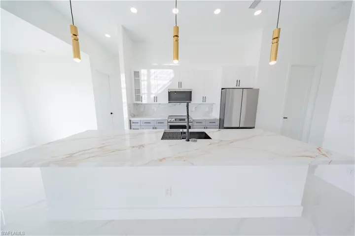 Kitchen with white cabinets, light stone countertops, a large island with sink, stainless steel appliances, and backsplash