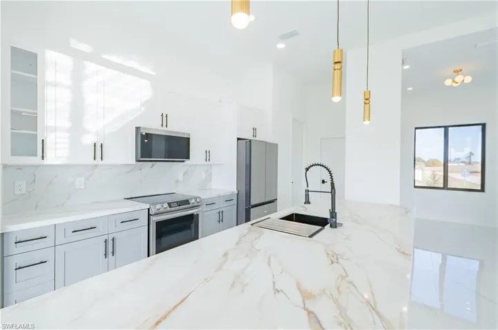 Kitchen featuring white cabinets, light stone counters, hanging light fixtures, and stainless steel appliances