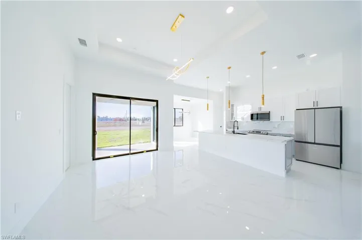 Kitchen with stainless steel appliances, white cabinets, an island with sink, tasteful backsplash, and decorative light fixtures