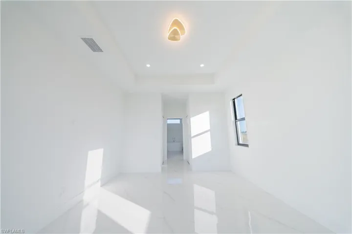 Spare room with recessed lighting, light marble finish flooring, and a raised ceiling