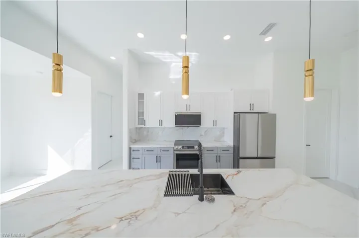 Kitchen featuring decorative light fixtures, light stone counters, white cabinetry, stainless steel appliances, and glass fronted cabinets
