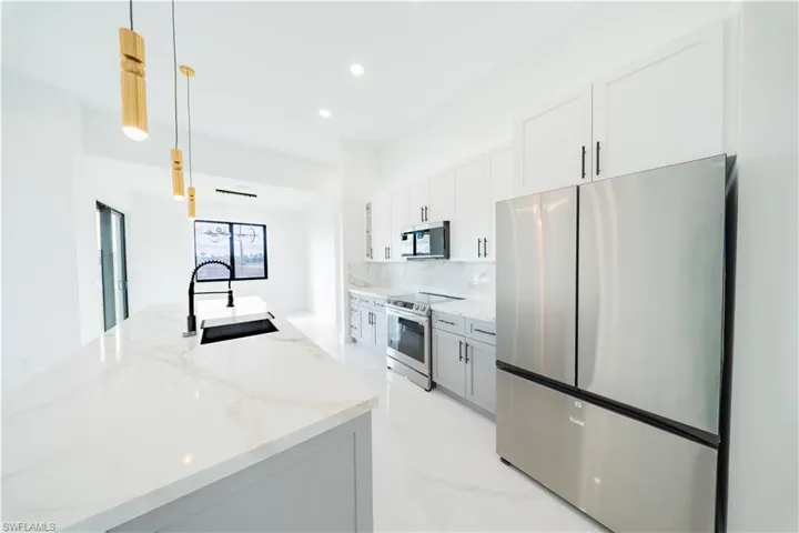 Kitchen featuring stainless steel appliances, decorative light fixtures, light stone countertops, a center island with sink, and light marble finish flooring