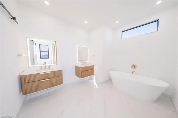 Bathroom with two vanities, recessed lighting, a soaking tub, and light marble finish floors