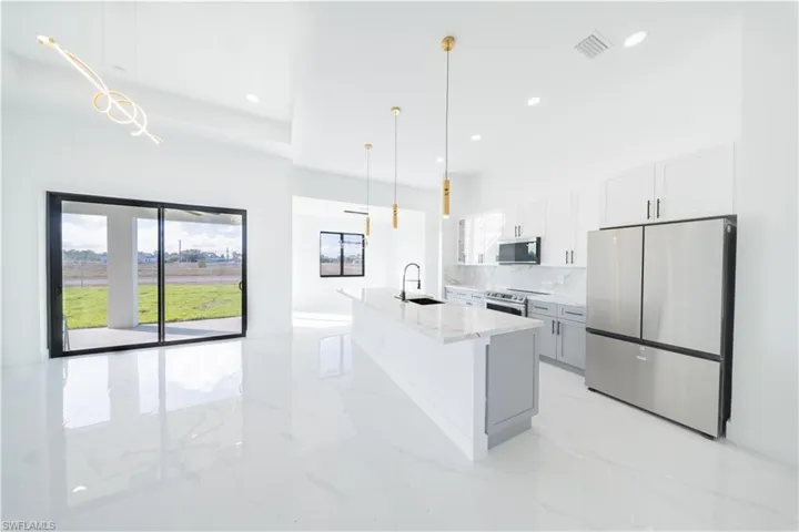 Kitchen with stainless steel appliances, light stone counters, white cabinetry, decorative light fixtures, and an island with sink