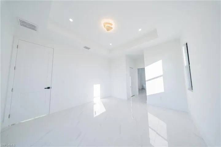 Unfurnished bedroom featuring recessed lighting, a tray ceiling, and light marble finish flooring