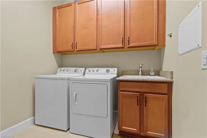 Dedicated laundry area featuring upper and lower wood-finish cabinetry, a utility sink with a stone-finish countertop, and a single-handle faucet