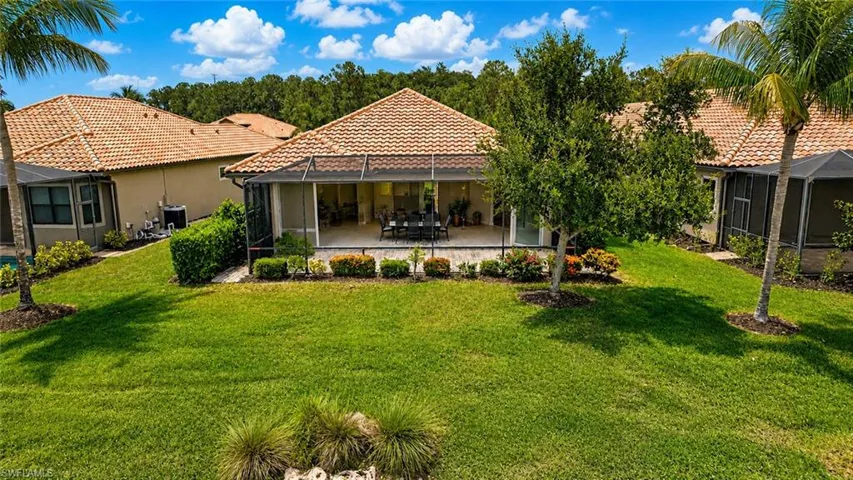Expansive rear exterior featuring a screened lanai with accordian shutters, tile roofing, stucco siding, and mature landscaping