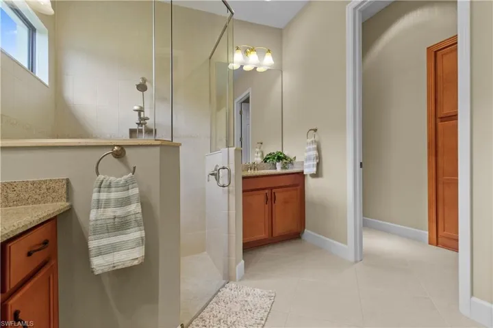 Spacious bathroom featuring a glass-enclosed shower with tiled walls, dual wood-finish vanity cabinets with granite-style countertops, and a full-height wood-finish storage cabinet