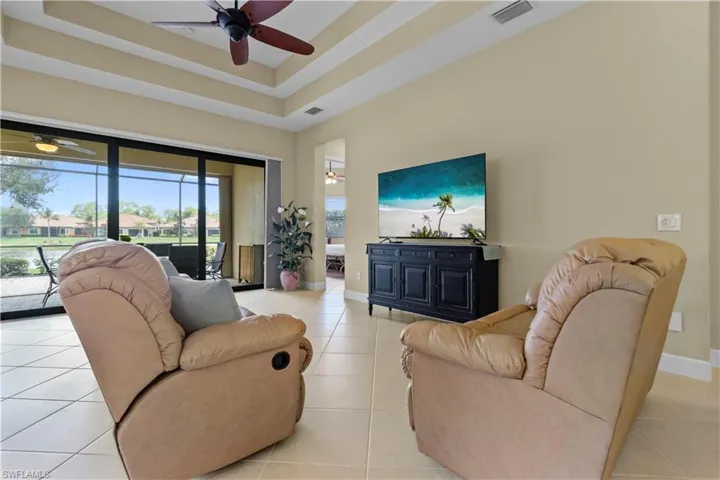 Living area with tray ceilings, ceiling fan, and large format tile flooring