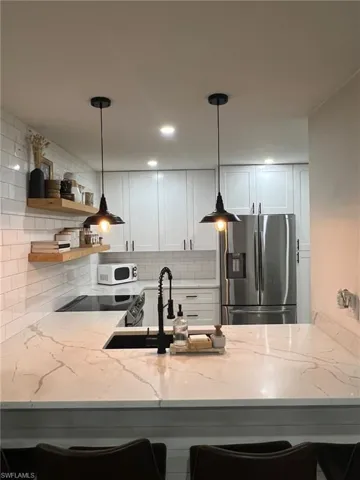Kitchen featuring white cabinetry, a subway tile backsplash, stainless steel appliances, and a countertop with integrated sink