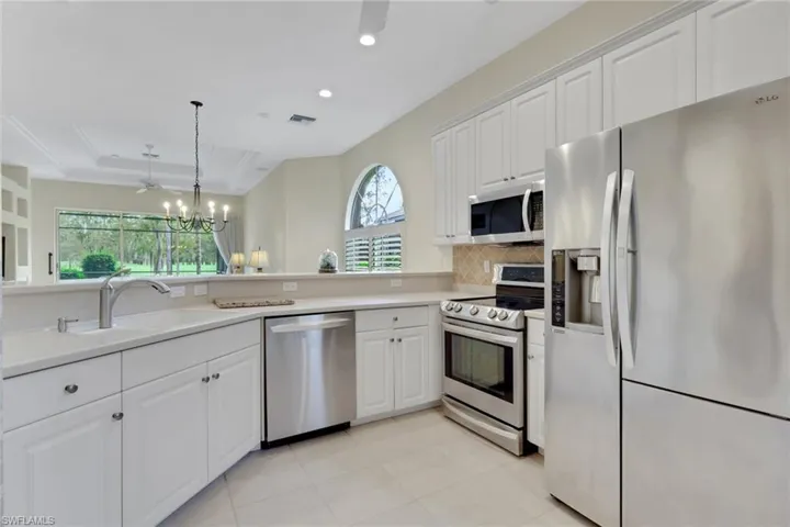 Kitchen with stainless steel appliances, white cabinets, a chandelier, light countertops, and recessed lighting