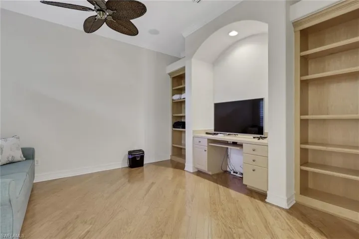 Unfurnished living room featuring built in shelves, built in desk, light wood-type flooring, and crown molding