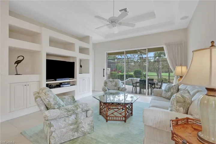 Living area with built in features, a raised ceiling, ceiling fan, tile patterned floors, and a sunroom