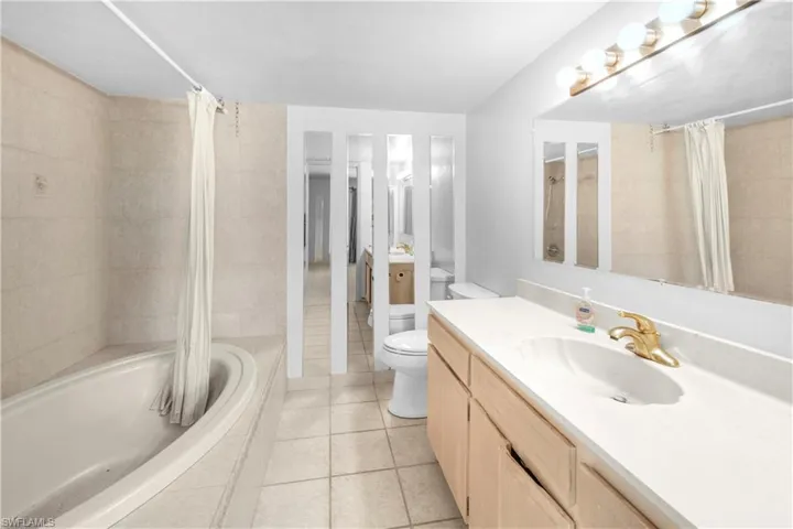 Full bathroom with shower / bathtub combination with curtain, vanity, toilet, and tile floors