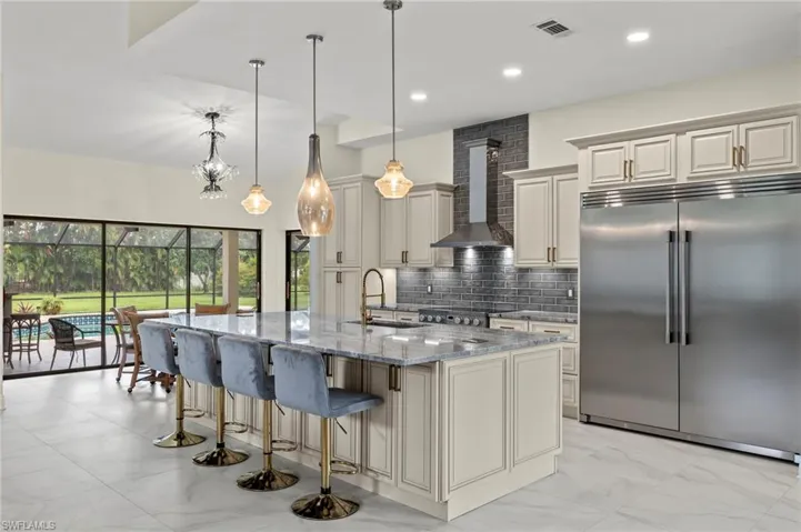 Kitchen with wall chimney exhaust hood, a sink, built in refrigerator, stone counters, and backsplash