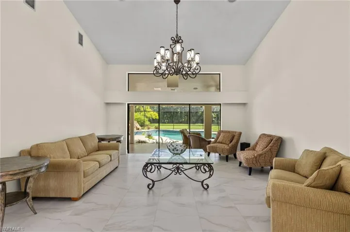 Living room with high vaulted ceiling, visible vents, marble finish floor, and an inviting chandelier