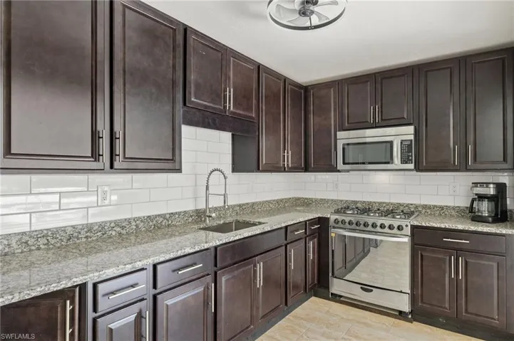 Kitchen with tasteful backsplash, appliances with stainless steel finishes, a sink, and light stone countertops