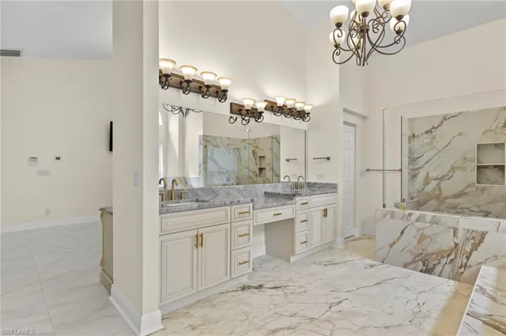 Bathroom with a chandelier, marble finish floor, a sink, double vanity, and baseboards