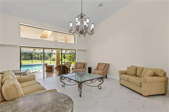 Living area with high vaulted ceiling, marble finish floor, and a notable chandelier