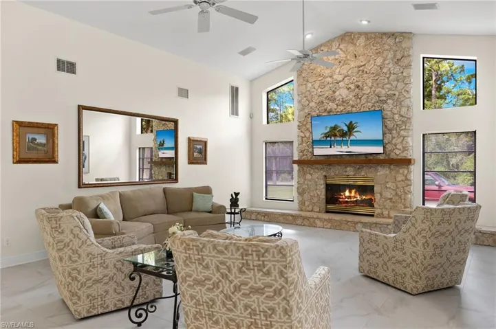 Living room with high vaulted ceiling, a ceiling fan, a stone fireplace, visible vents, and marble finish floor