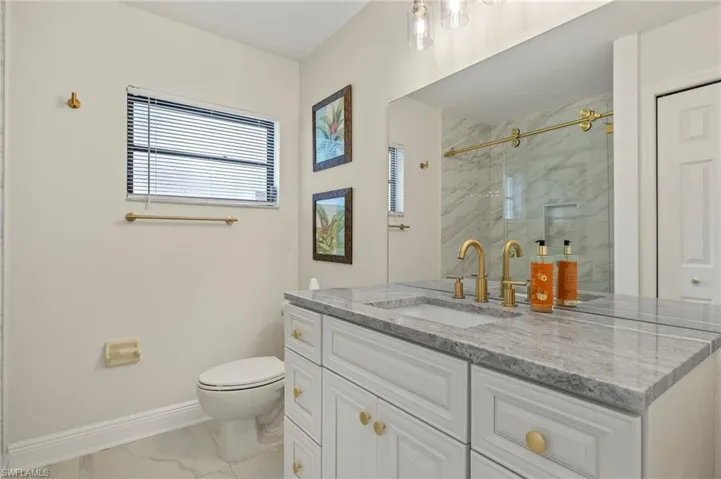 Full bath featuring baseboards, toilet, an enclosed shower, vanity, and marble finish floor